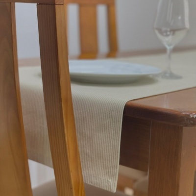 Mesa de madeira clara com toalha bege, prato branco e copo transparente