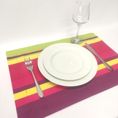 Conjunto de talheres, pratos e copo sobre individual colorido com riscas horizontais
