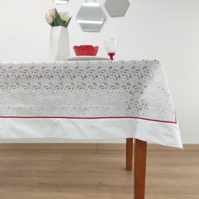 Toalha de mesa branca com bordado floral e decoração vermelha sobre mesa de madeira com vaso, prato e copo