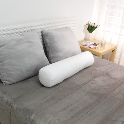 Cama com colcha cinzenta, almofadas cinzentas e branca cylindrical, cabeceira branca e mesa de cabeceira de madeira com flores.