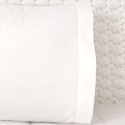 Almofada branca com costura decorativa sobre cama clara texturizada