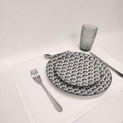 Serviço de mesa com pratos decorados, talheres prateados e copo texturizado sobre toalhete branco