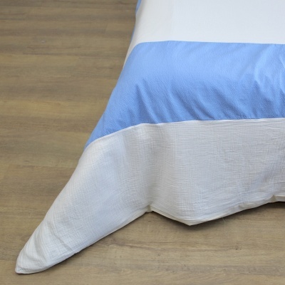 Colcha azul e branca com textura sobre chão de madeira clara