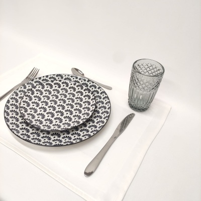 Conjunto de jantar com pratos estampados, talheres de metal e copo de vidro cinzento sobre toalha branca