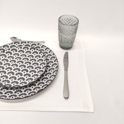 Pratos com padrão floral preto e branco, talheres prateados, copo de vidro texturizado sobre guardanapo branco