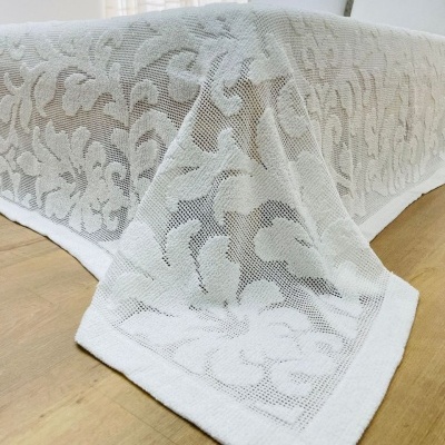 Colcha branca com padrão floral em relevo sobre cama com almofadas brancas