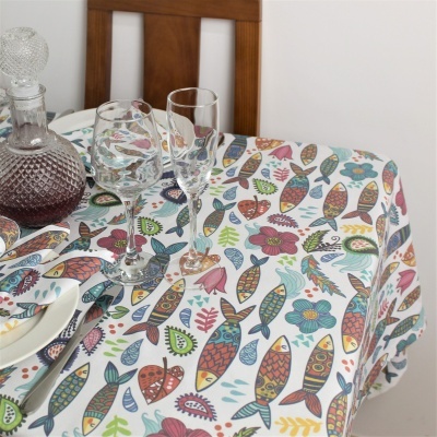 Toalha de mesa com padrão colorido de peixes e flores em mesa de madeira com taças e decantador de vidro
