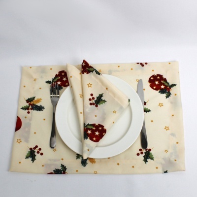 Guardanapo e toalha de mesa creme com motivos natalícios vermelhos, verdes e dourados, prato branco, faca e garfo
