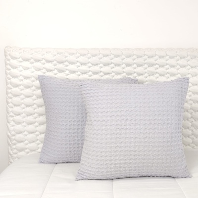 Almofadas cinzentas texturizadas em cama branca com cabeceira matelassada