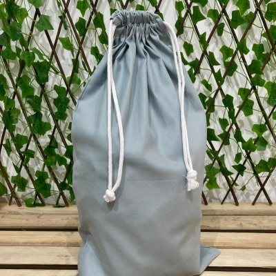 Saco de pano cinzento com cordão branco, madeira clara e treliça com folhas verdes