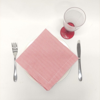 Prato branco com guardanapo riscado vermelho, talheres de metal e copo com base vermelha