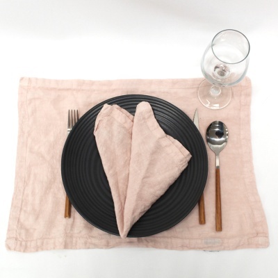 Conjunto de mesa com prato preto, guardanapo rosa em forma de coração, talheres de cabo de madeira e copo de vidro