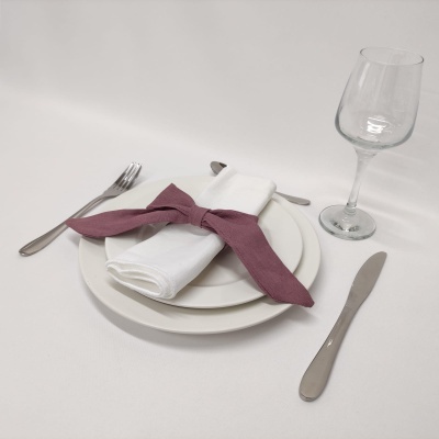 Mesa posta com pratos brancos, guardanapo com laço roxo, talheres de aço inox e copo de vidro