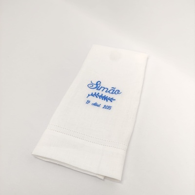 Guardanapo de pano branco com bordado azul a dizer Simão e data 19 abril 2025