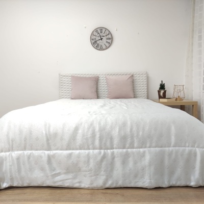 quarto com cama branca e almofadas cor de rosa, relógio de parede e mesa de cabeceira com planta