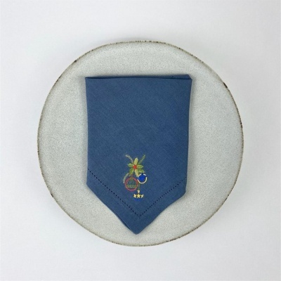Guardanapo azul escuro com bordado colorido sobre prato cinza claro