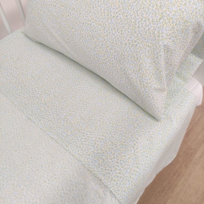 Conjunto de roupa de cama com padrão floral amarelo e azul sobre branco numa cama branca.