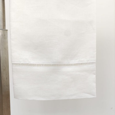 Toalha branca com detalhe bordado pendurada numa superfície de madeira clara