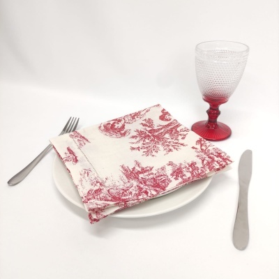 Conjunto de mesa com prato branco, guardanapo branco e vermelho, talheres metálicos e copo de vidro vermelho e transparente