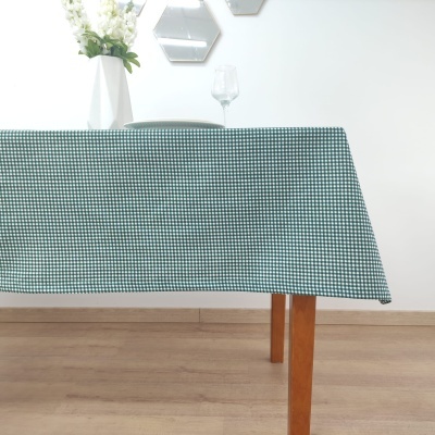 Toalha de mesa verde com padrão de quadrados pequenos numa mesa de madeira com vaso branco e taça