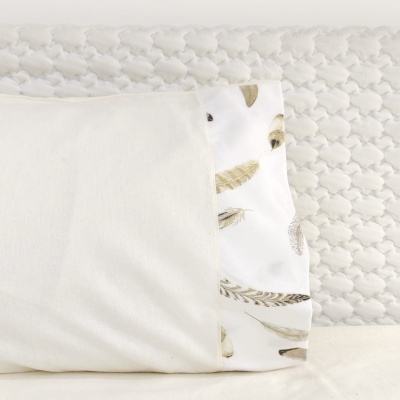 Coussin branco com estampa bege e cinza e fundo branco, sobre superfície com padrão acolchoado branco.