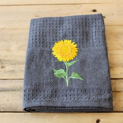 Toalha cinza escura com bordado de girassol sobre madeira clara