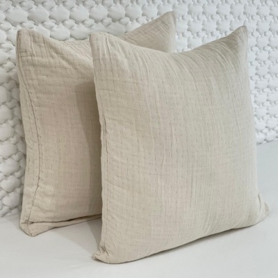 Duas almofadas quadradas bege claro sobre superfície branca com parede texturizada