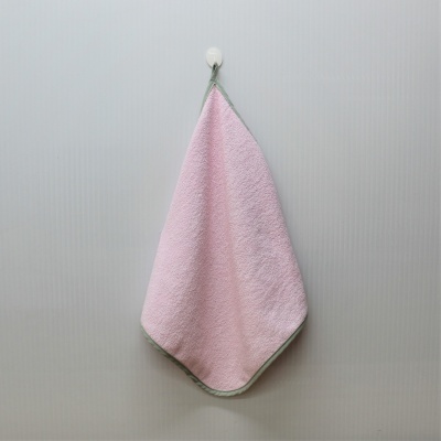 Toalha de mão rosa com borda verde pendurada numa parede cinza