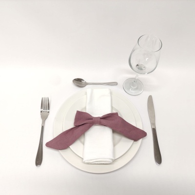 Conjunto de mesa com prato branco, guardanapo com laço vinho, talheres metálicos e copo de vidro