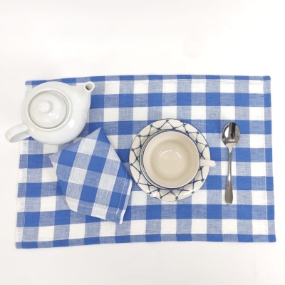 Conjunto de chá com bule branco, chávena e pires creme e azul, colher de metal, guardanapo e individual xadrez azul e branco