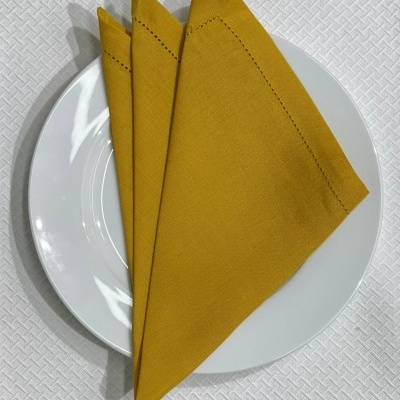 Guardanapo amarelo tecido sobre prato branco numa mesa com toalha branca texturizada