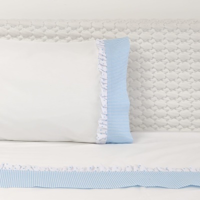 Capa de edredão e almofada branca com detalhes azuis e folhos, cabeceira branca acolchoada.