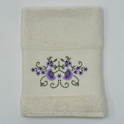 Toalha creme com bordado floral lilás e verde num fundo branco