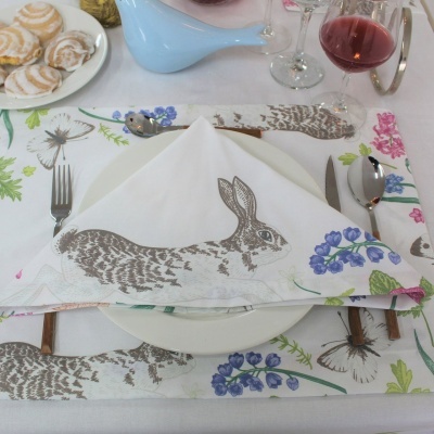 Mesa posta com guardanapo e individual de tecido estampados com coelho e flores, talheres, taças e doces