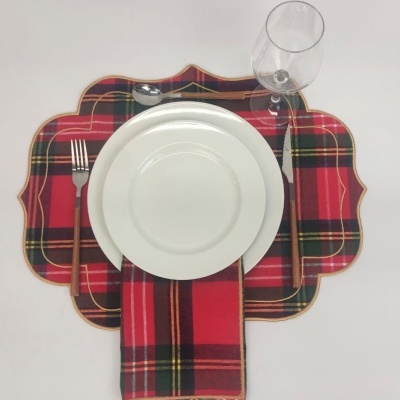 Conjunto de mesa com sousplat e guardanapo xadrez em tons vermelhos, prato branco, talheres de cabo de madeira e copo de vidro