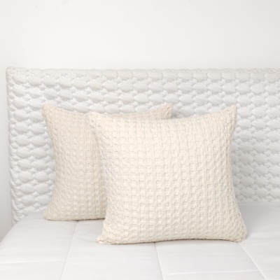 Duas almofadas brancas texturizadas sobre cabeceira acolchoada branca