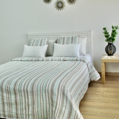 Quarto com cama e roupa de cama de riscas cinza e branca, mesa de cabeceira de madeira, jarro preto com plantas e decoração na parede branca