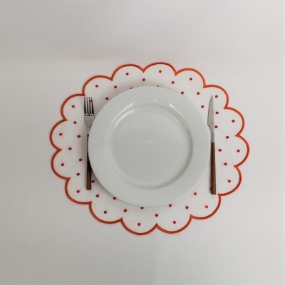 Prato branco redondo sobre sousplat branco com bordas onduladas e pontos vermelhos, garfo e faca ao lado