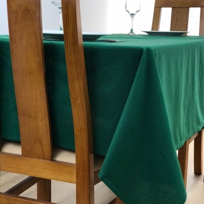Toalha de mesa verde escuro sobre mesa de madeira com cadeiras, copos e pratos num ambiente interior