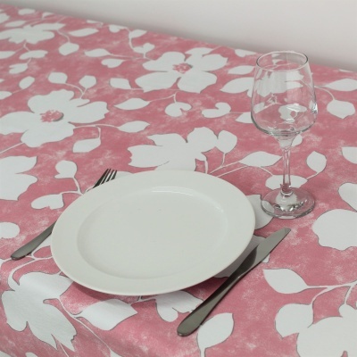 Mesa posta com toalha rosa com flores brancas, prato branco, talheres e taça