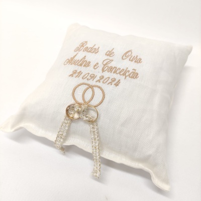 Almofada branca bordada com texto e dois anéis dourados entrelaçados com cristais