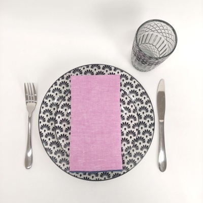 Conjunto de prato decorativo com guardanapo rosa, talheres de metal e copo de vidro transparente.