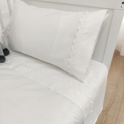 Jogo de cama branco com bordado rendado numa cama branca