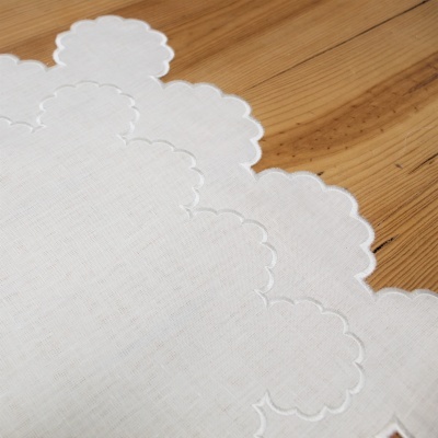 Pano branco de tecido com bordas bordadas sobre madeira clara