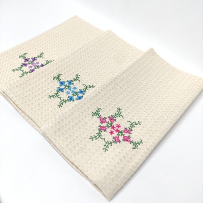 Três panos de cozinha beges com bordado floral colorido