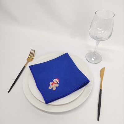 Conjunto de loiça com pratos brancos, guardanapo azul com boneco de gengibre, talheres preto e dourado e copo de vinho transparente