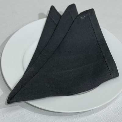 Três guardanapos de tecido pretos dobrados em prato branco sobre toalha branca