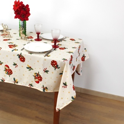 Toalha de mesa natalícia creme com estampado de botas vermelhas, folhas verdes e estrelas douradas sobre mesa de madeira, com pratos, copos e flores