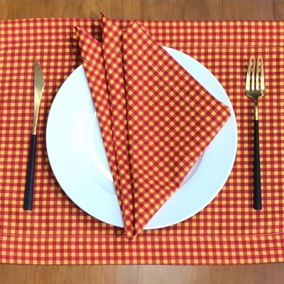 Toalha e guardanapo vermelho com amarelo, prato branco, faca e garfo dourados com cabos pretos