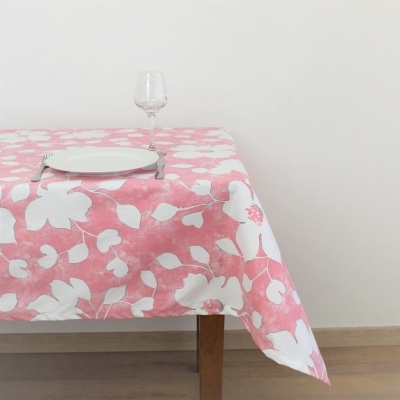 Toalha de mesa rosa com flores brancas, prato branco, talheres e taça numa mesa de madeira